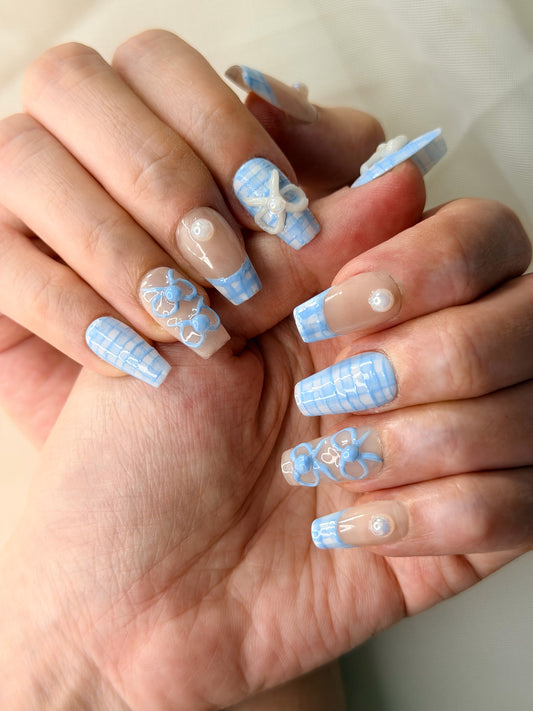 A close-up of hands showcasing a cottage nail art design with plaid patterns and white bowtie.