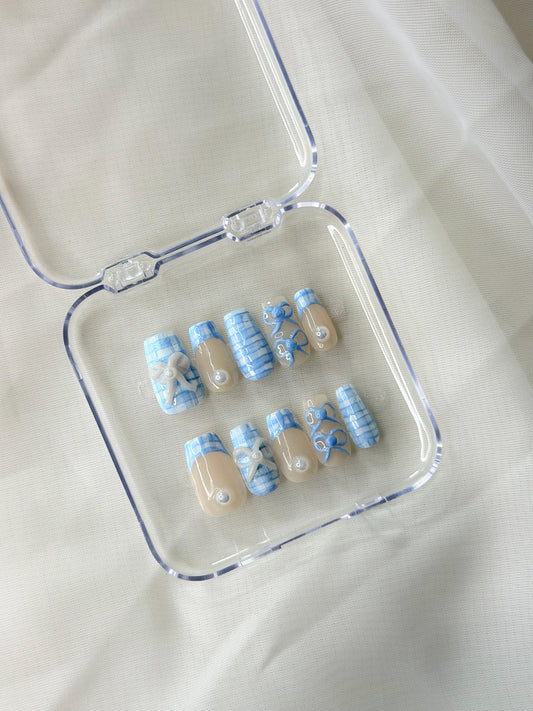A set of 10 press-on nails with a blue and white patterned design and beige tips, displayed inside a clear plastic case.