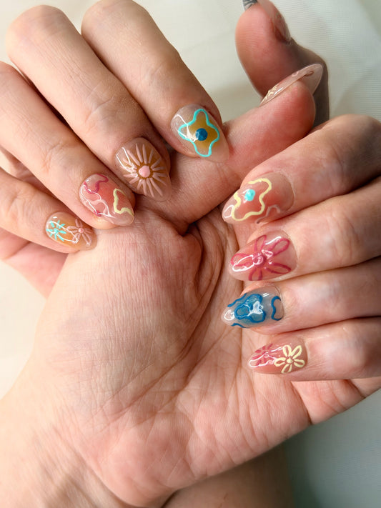 Close-up of a person's hands showcasing colorful nail art designs with floral and geometric patterns on clear press-on nails.