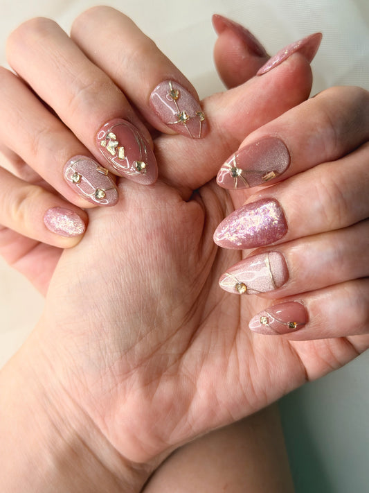 Close-up of hands showcasing a manicure with glossy pink and nude almond-shaped nails decorated with small gold rhinestones and glitter.