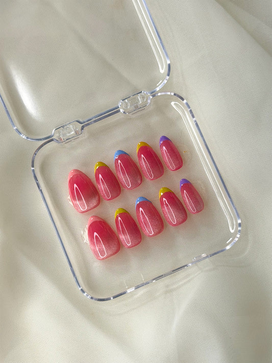 A set of cat-eye glossy pink press-on nails with colorful gradient tips, displayed inside a clear plastic case.